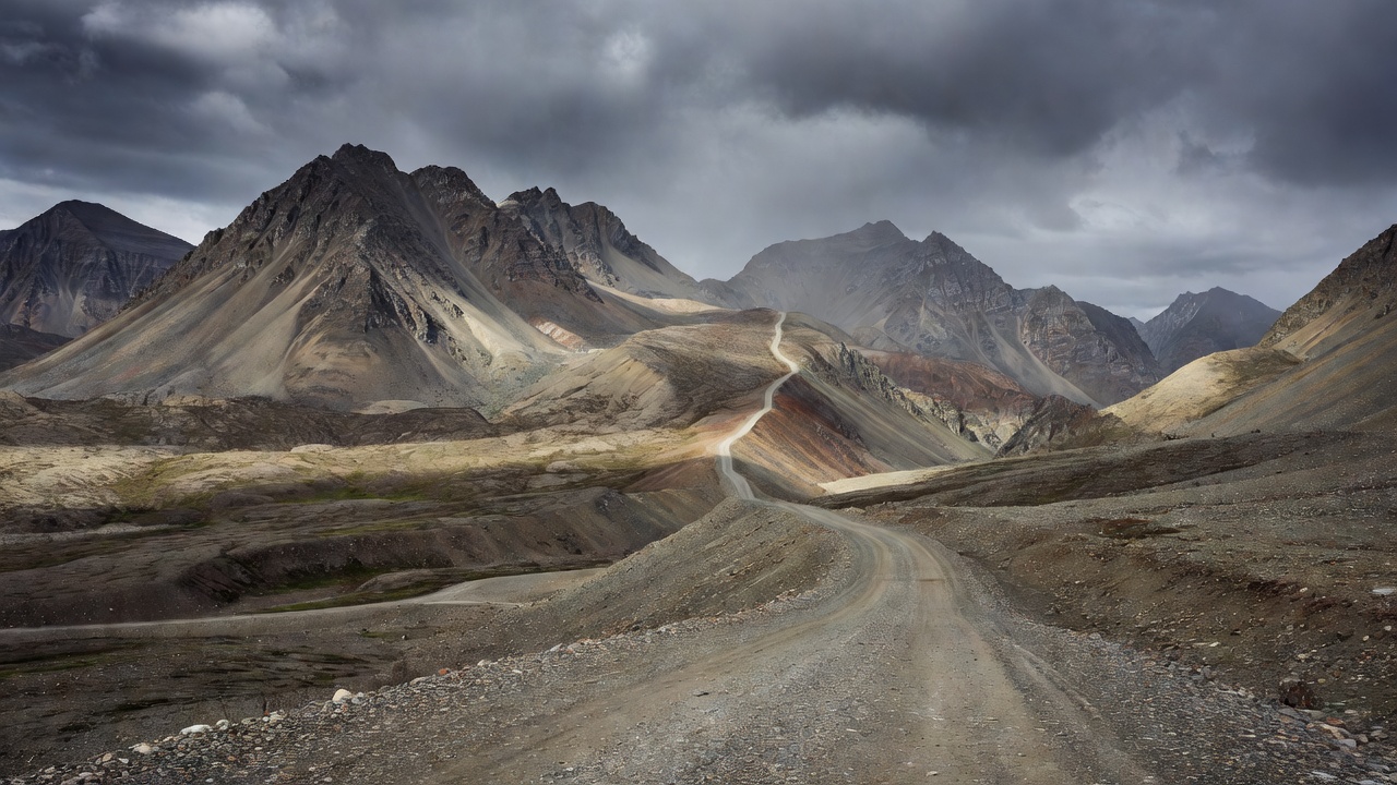 Gravel Dalton Highway climbing toward Atigun Pass through the bare peaks of the Brooks Range