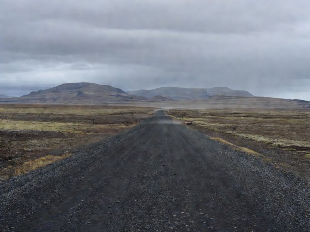 Dark shale surface of the Dempster Highway stretching across tundra with low mountains behind