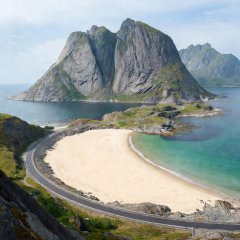 Bend on the E10 in Lofoten beside a sandy bay below granite peaks